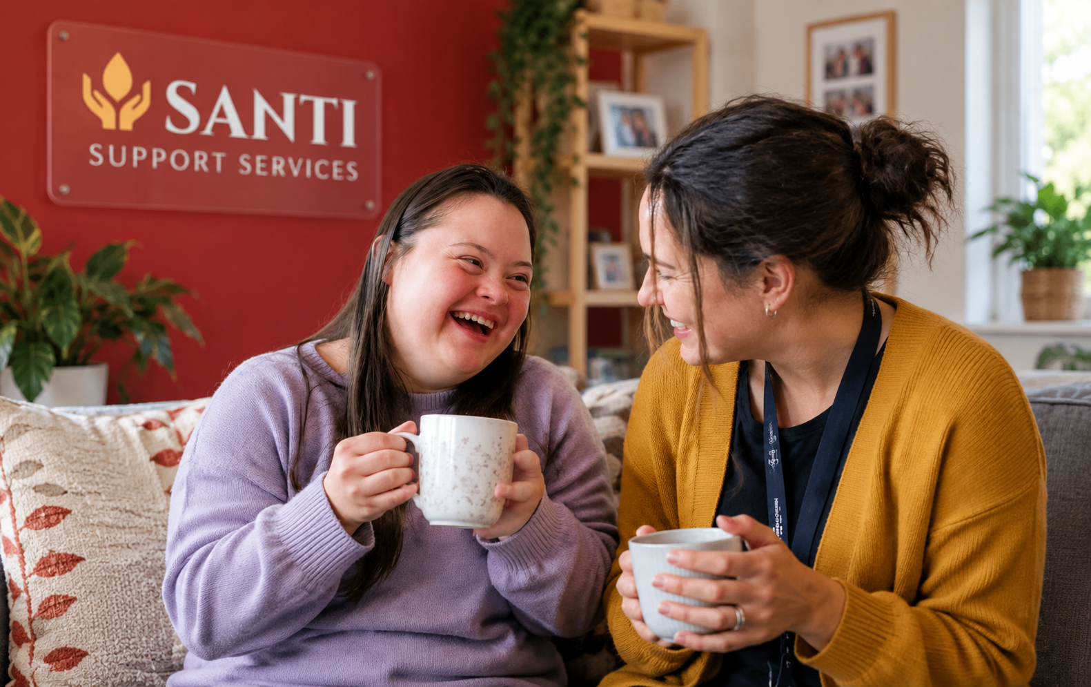 A participant and support worker laughing together over coffee at home