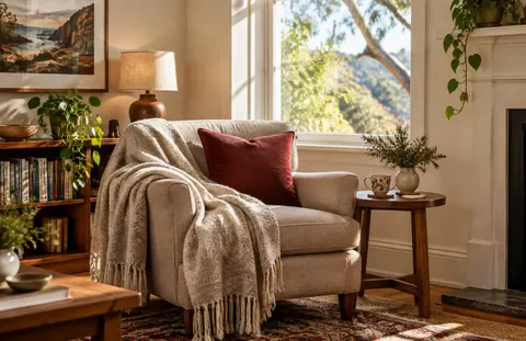 A cosy armchair with a blanket and a cup of tea by the window in warm light