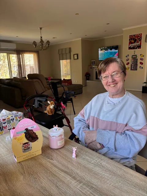 A smiling woman at a table with gifts and a celebration cake