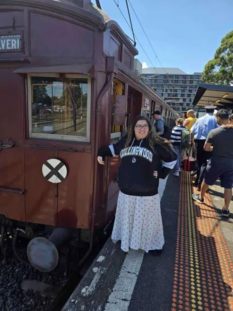 A smiling woman beside a heritage train on an outing
