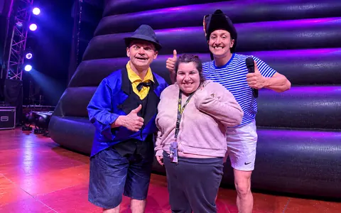 A woman smiling between two performers on a theatre stage